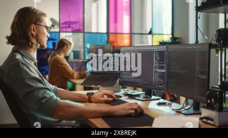 Caucasian Man Coding on Personal Computer and Laptop Set Up In Stylish Office. Professional Programmer Developing Innovative AI Software in Technological Start-Up, Using Multiple Displays. Stock Photo