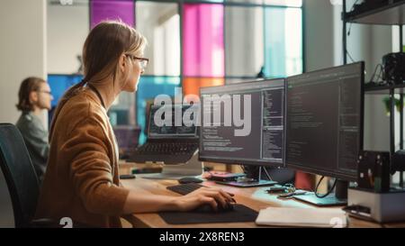 Female Software Engineer Writing Code on Desktop Computer with Multiple Screens Setup in Stylish Coworking Office Space. Professional Caucasian Woman Working on SaaS Platform For Innovative Startup. Stock Photo