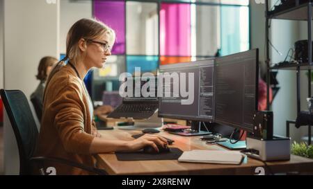 Caucasian Woman Coding on Desktop PC and Laptop Setup With Multiple Displays in Spacious Office. Female Junior Software Engineer Working on New Sprint of Mobile Application Development For Start-up. Stock Photo