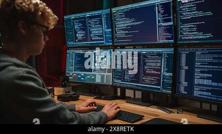 Young Caucasian Man Writing Code on Professional Six Monitors Setup in Dark Office. Male Cyber Security Expert Controlling Digital Data Protection System in International Intelligence Agency. Stock Photo