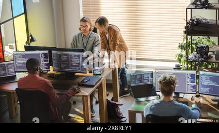 Creative Office: Diverse Colleagues Coding on Desktop Computers With Multiple Monitors. Female Project Manager Talks to Male Team Lead While Junior Developers Working on Mobile Application. Stock Photo