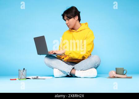 Young Guy Working on Laptop in Studio With Blue Background Stock Photo
