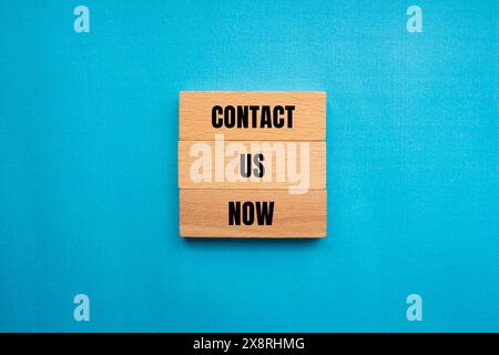 Contact us now words written on wooden blocks with blue background. Conceptual contact us now symbol. Copy space. Stock Photo
