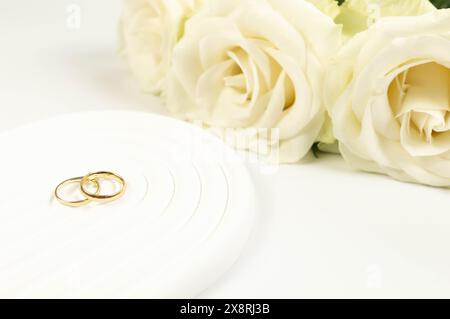 Wedding white roses and gold wedding rings on white background. Wedding composition, white arch tray, podium. Copy space, flat lay. Stock Photo