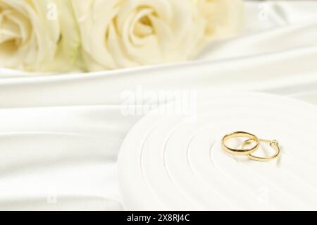 Wedding white roses and gold wedding rings on white silk background. Wedding composition, white arch tray, podium. Copy space, flat lay. Stock Photo