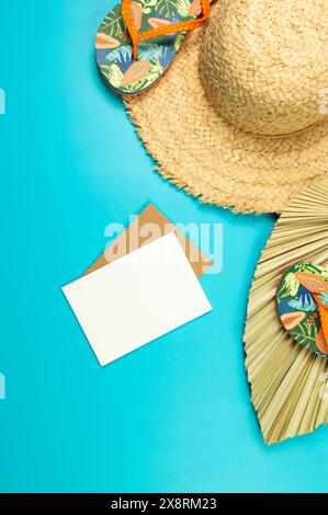 Top view of straw hat, dried palm leaf, white card and slippers on blue background. Summer fashion, vacation and beach wallpaper. Copy space, flat lay. Stock Photo