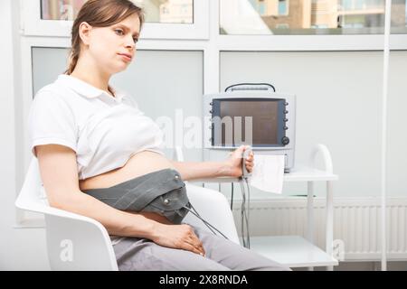 A pregnant woman performing cardiotocography (CTG) to monitor fetal heartbeat and uterine contractions during the final weeks of pregnancy Stock Photo