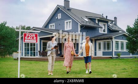 Excited Young Couple Chatting with Happy Real Estate Agent. Businesswoman Talking About the House with Young Man and Pregnant Female. Standing on a Lawn Next to For Sale Sign on a Warm Day. Stock Photo