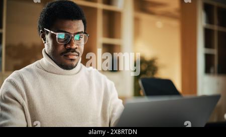 Portrait of Black Productive Young Man Working on Laptop in a Cotemporary Office. Businessman Developing an E-commerce Strategy and Brainstorming. He is Thinking and Typing Stock Photo