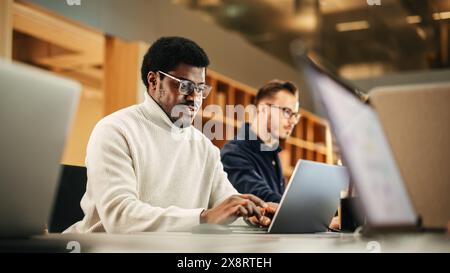 Portrait of Enthusiastic Black Man Turning on his Laptop and Starting his Work Day at the Office. Male Graphic Designer Smiling While Developing a New Visual Concept Stock Photo
