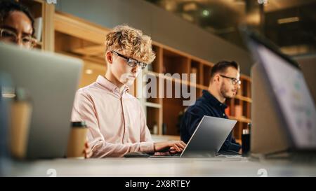 Diverse Multiethnic Creative Team Working On Laptops in Bright Busy Office. Portrait of Young Caucasian Man Using Laptop and Smiling. Male Developer Engineering a Software Stock Photo
