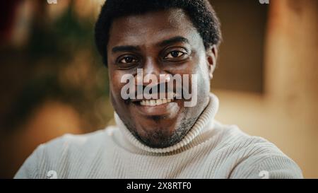 Close-up Portrait of Handsome Black Man with Trimmed Beard, Wearing Stylish White Turtleneck, Smiling and Looking at the Camera. Confident Male Startup CEO Celebrating his Achievement Stock Photo