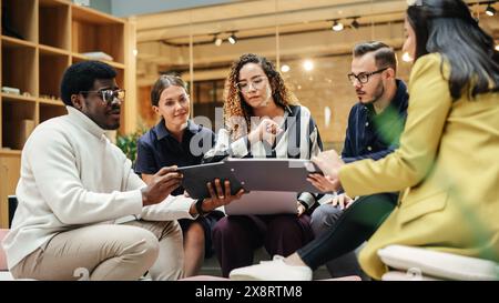Group of People from Multiple Ethnicities Working on Problem Solving Using Notes, Laptop and Tablet in a Meeting Room at the Office. Teammates Giving Constructive Feedback on Eachother's Projects Stock Photo