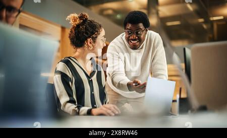 Portrait of Two Creative Young Colleagues Consulting Eachother Using Laptop in Modern Office. Black Male Supervisor Discussing Scheduling with Female Hispanic Head of Operations.. Stock Photo