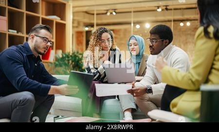 A Group of Multiethnic People Brainstorming Using Laptop and Charts in a Meeting Room at Office. Enthusiastic Young Adults Analyzing New Data To Improve Startup Performance. Medium Shot Stock Photo