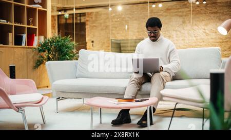 Portrait of Focused Black Man Working on a Laptop in a Meeting Room at Office. Dedicated Male Web Developer Optimizing SAAS system. Cyber Security Specialist Checking Startup Website Protocol Stock Photo