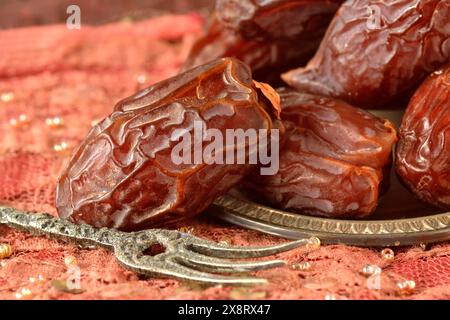 Dried dates in metal saucer plate with small fork Stock Photo