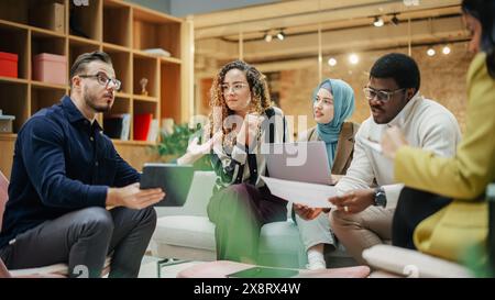 Group of Young Multiethnic People Working Together Using Laptop, Tablet and Charts in a Meeting Room. Energetic Teammates in a Meeting Room in an Office, Analyzing Statistics and Reviewing Data Stock Photo