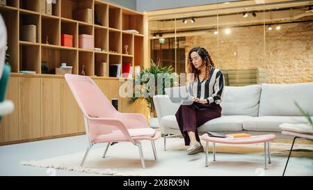 Portrait of Hispanic Creative Young Woman Working on a Laptop in Casual Office. Female Team Lead Smiling While Checking her Team Performance Data. Focused Hard Worker. Wide Shot Stock Photo