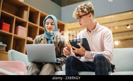 Portrait of Two Creative Colleagues Collaborating and Working with the Laptop in Modern Office. Muslim Female Manager Consults White Project Manager, They Brainstorm on the Project Stock Photo