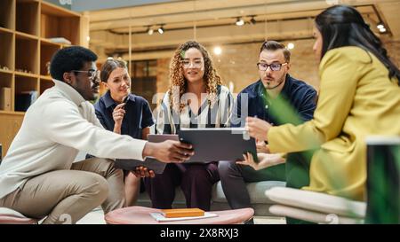 Multiethnic Group of Creative People Working on Project in a Modern Bright Office. A Diverse Group of Colleagues Developing a New Approach Using Charts, Laptop, and Tablet. Wide Shot Stock Photo