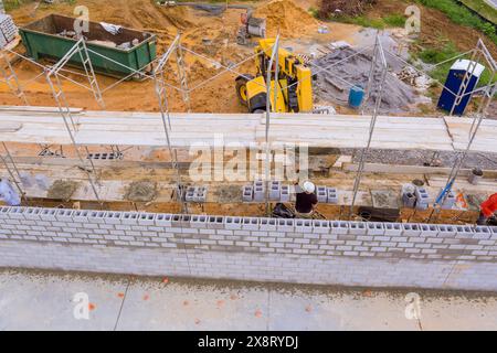 On construction site, mason stands on scaffolding constructs concrete wall using cement blocks Stock Photo