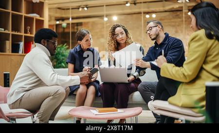 Multi Ethnic Group of People Working on Developing Growth Ideas Based on Data. Energetic Teammates in a Meeting Room in an Office, Analyzing Charts Using Tablet and Laptop. Wide Shot Stock Photo