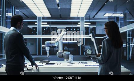 Young Female Engineer Works with Colleague Scientist. They Collaborate on a Robot Arm Development, Research and Manufacture Project. Analyzing and Evaluating Technology and Kinetic System. Stock Photo