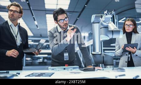 Team Leader Working with Robotics Engineers on a Robot Arm Project, Discussing the Project in Scientific Technology Lab. Young Team Researching and Developing an AI Robotic Arm in Industrial Facility. Stock Photo