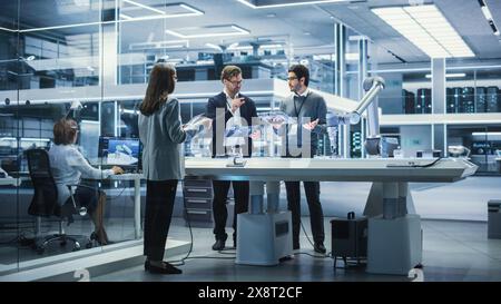 Robotics Engineer, Project Manager and Machinery Operator Collaborate on a Robot Arm Project, Standing with Tablet Computers in Scientific Technology Lab. Young Team Developing an AI Robotic Arm. Stock Photo