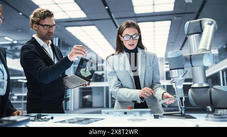 Team Leader Working with Robotics Engineers on a Robot Arm Project, Discussing the Project in Scientific Technology Lab. Young Team Researching and Developing an AI Robotic Arm in Industrial Facility. Stock Photo