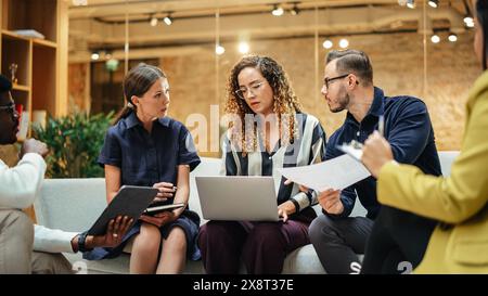 Multiethnic Group of People Brainstorming in a Meeting Room at the Office. Teammates From The Marketing Department Working on a New Campaign Using Laptop and Tablet. Stock Photo