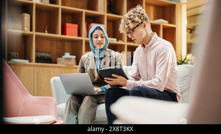 Two Creative Colleagues Collaborating Over a Work Project Using Computer and Tablet at Office. Male E-commerce Marketing Manager Discussing with Muslim Female Media Planner. Medium Stock Photo