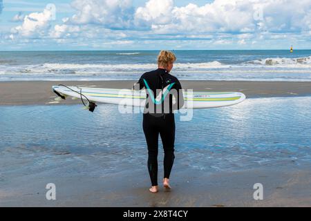 Woman going surfing Hook of Holland, Netherlands. Female surfer walking into the North Sea and it s surf, wearing a wetsuit. Hoek van Holland Strand Zuid-Holland Nederland Copyright: xGuidoxKoppesxPhotox Stock Photo