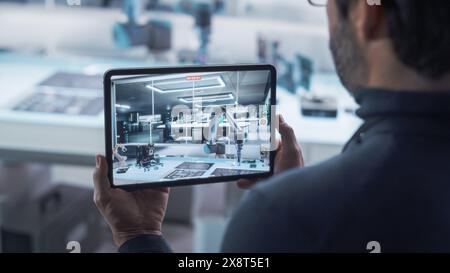 Over the Shoulder Shot of a Robotics Engineer Using a Tablet Computer Running Augmented Reality Software. Robotic Arm Holding a Microchip. Automation Startup Research and Development Office. Stock Photo