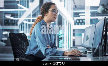 Happy Multiethnic Female Industrial Engineer Developing 3D Model of a Circuit Motherboard on Computer CAD Software in a Startup Facility. Modern Technological Research and Development Center. Stock Photo