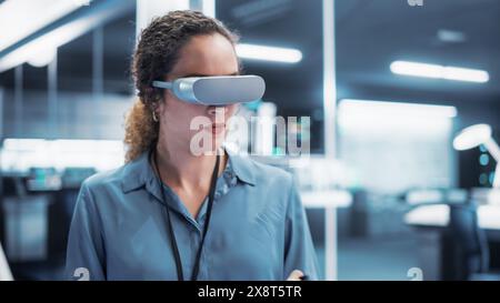 Portrait of a Female Engineer Using a Futuristic Virtual Reality Headset with Controllers to Operatean Indsutrial Robot or Spend Time in Virtual Office Metaverse. Stock Photo