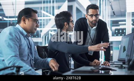 Team of Three Industrial Design Agency Specialists Discussing a 3D Circuit Board Model Created on a CAD Software on Desktop Computer. Young Smart Multicultural Men Working in Electronics Factory. Stock Photo