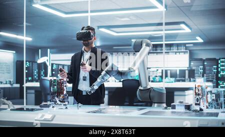 Robotics Engineer Operating a Futuristic Robotic Arm, Using a Virtual Reality Headset and Controllers to Perform Tasks. Work in Research and Development High Tech Facility Startup. Stock Photo