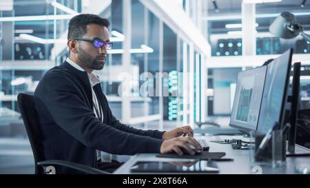 Portrait of a Handsome Hispanic Industrial Engineer Developing 3D Model of a Circuit Motherboard on Computer CAD Software in a Factory. Modern Technological Research and Development Center. Stock Photo
