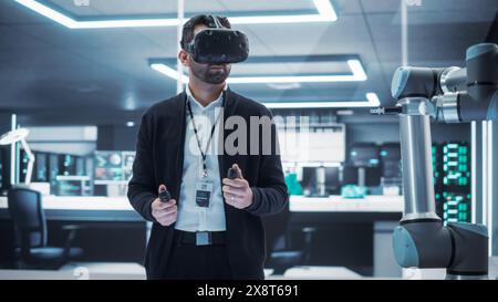 Robotics Engineer Operating a Futuristic Robotic Arm, Using a Virtual Reality Headset and Controllers to Perform Tasks. Work in Research and Development High Tech Facility Startup. Stock Photo