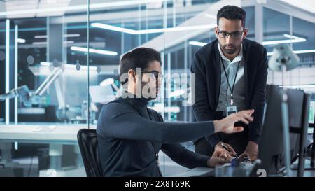 Portrait of Two Young Multiethnic Software Interface Programmers Chatting and Using a Computer with CAD Model of a Prototype Circuit Motherboard with Microchips, Capacitors, Transistors and Inductors. Stock Photo