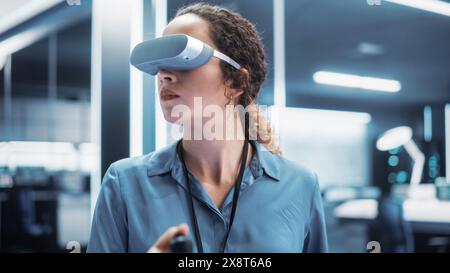 Portrait of a Female Engineer Using a Virtual Reality Headset with Controllers to Operatean Indsutrial Robot or Spend Time in Virtual Office Metaverse. Stock Photo
