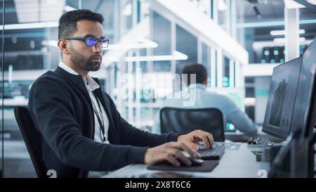 Portrait of Multiethnic Industrial Engineer Developing 3D Model of a Circuit Motherboard on Computer CAD Software in a Factory. Modern Technological Research and Development Center. Stock Photo