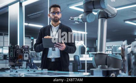 Industrial Robotics Professional Interacting with Robotic Arm During a Research Phase in a High Tech Startup. Scientist Uses Tablet Computer to Manipulate and Program the Robot to Move a Microchip. Stock Photo