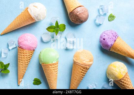 Various ice cream scoops in cones on blue background,  top view. Assortment of vegan colorful ice cream in waffle cones. Flat lay. Stock Photo