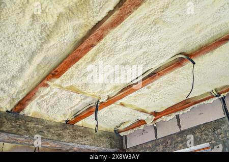 Insulation of the ceiling in the house with polyurethane foam. Insulating foam between wooden beams Stock Photo