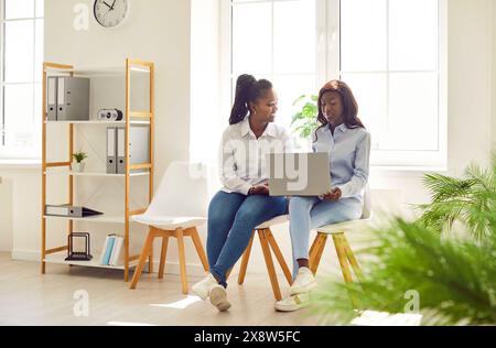 Young business women having meeting at office sitting on chairs with laptop and talking. Stock Photo