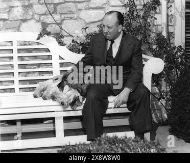 Film Director ALFRED HITCHCOCK photographed ini the garden of his Hollywood home in Bel Air, Los Angeles in 1945 sitting on a bench with his two dogs Johnny, a Sealyham and Edward, a Cocker Spaniel. It was taken at the time that he was making SPELLBOUND with INGRID BERGMAN and GREGORY PECK. Selznick International Pictures / Vanguard Films Stock Photo