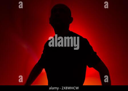 Studio portrait of a man in silhouette, standing still and posing. Isolated on red background. Stock Photo